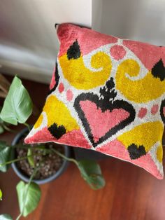 a pink and yellow pillow sitting on top of a wooden floor next to a potted plant