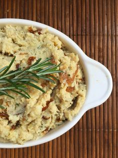 a bowl filled with mashed potatoes and topped with a sprig of rosemary