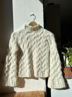 a white sweater is hanging on a wooden hanger next to a potted plant