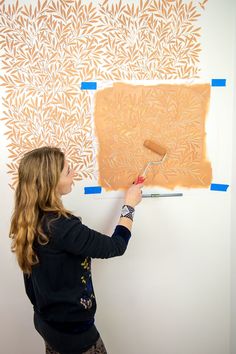 a woman is painting on the wall with blue tape