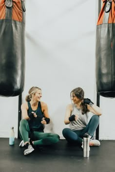 two women sitting on the ground in front of punching bags