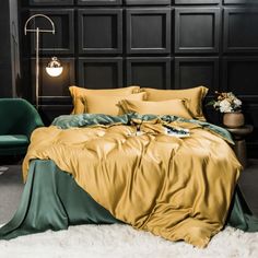 a bed with gold and green sheets in a black room next to a chair, table and lamp