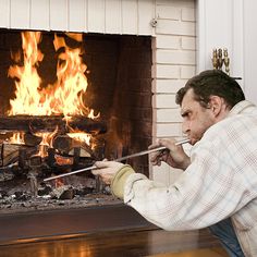 a man sitting in front of a fire place holding a pair of tongs up to his mouth