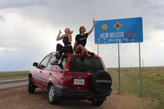 two women sitting on the roof of a red car in front of a new mexico sign