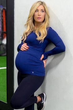 a pregnant woman leaning against a wall with her hands on her hips and looking at the camera