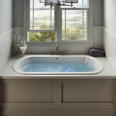 a bath tub sitting under a window next to a sink and counter top in a bathroom