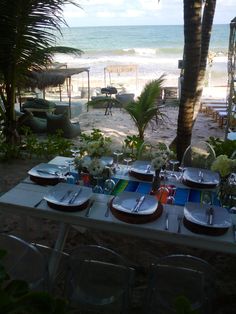 the table is set with plates and silverware for an outdoor dinner on the beach