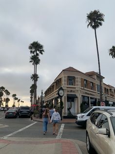 two people walking down the street in front of a building with palm trees on both sides