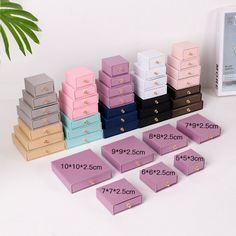 many different colors and sizes of jewelry boxes on a white table next to a plant