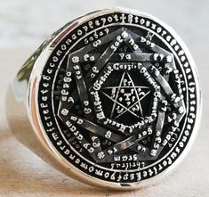 a silver ring with an intricate design on the front and center, sitting on a marble surface