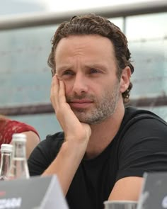 a man sitting at a table with his hand on his face and looking off to the side