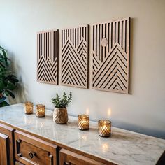 some candles are sitting on a marble counter top next to two wooden wall art pieces