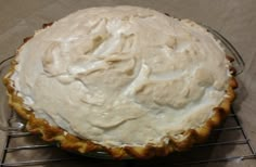 a pie sitting on top of a metal rack next to a pan filled with white frosting