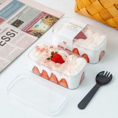 two plastic containers with strawberries in them next to a fork and newspaper on the table