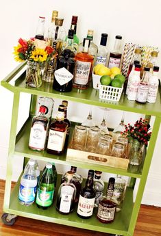 an assortment of liquor bottles and glasses on a green bar cart with flowers in vases