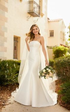 a woman in a white wedding dress holding a bouquet and posing for the camera with her hand on her hip