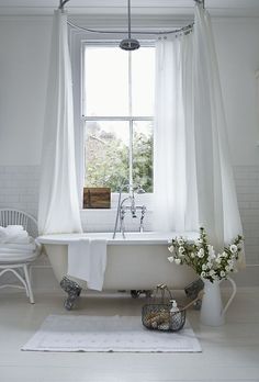 a white bath tub sitting under a window next to a vase with flowers in it