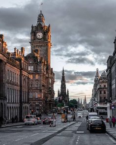 cars driving down the street in front of tall buildings with a clock tower on top