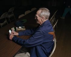 an older man sitting at a table with several items on it