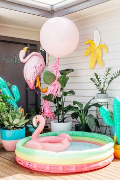 an inflatable pool with flamingos and balloons on the ground next to potted plants