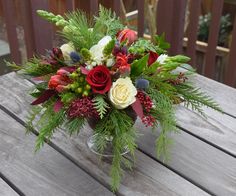 a vase filled with flowers and greenery on top of a wooden table