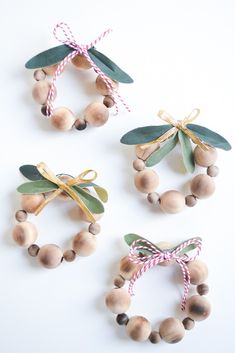 three small wooden beads with green leaves and ribbons tied around them on a white surface