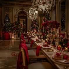 a table set for christmas dinner with red and gold decorations on the walls, candles and trees