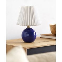 a blue lamp sitting on top of a wooden table next to a bowl and book