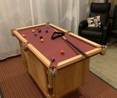 a pool table in the middle of a living room with a chair and couch behind it