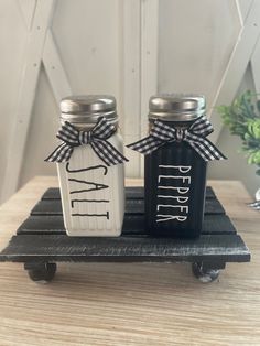 two salt and pepper shakers sitting on top of a wooden tray with a bow