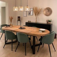 a dining room table with green chairs and lights hanging from the ceiling, along with pictures on the wall