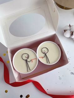 two buttons with faces drawn on them sitting in a box next to a red ribbon