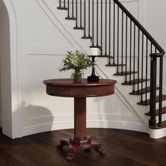 a vase with flowers sitting on top of a wooden table in front of a stair case