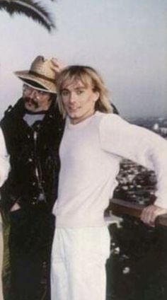 two men and a woman standing next to each other on a balcony with palm trees in the background