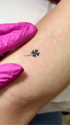 a person with pink gloves on their arm holding a small black four leaf clover tattoo