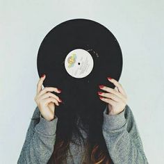 a woman covering her face with a vinyl record in front of her head, against a white background