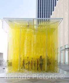 a yellow sculpture in front of a tall building