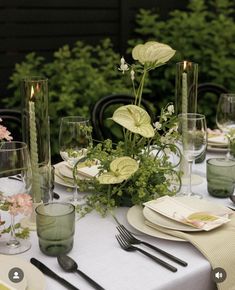 the table is set with plates, silverware and green flowers in vases on it