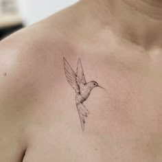 a small tattoo on the chest of a woman with a hummingbird flying above it