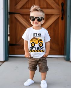 a little boy that is standing in front of a door wearing sunglasses and a t - shirt