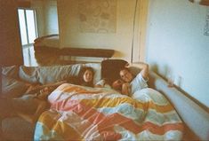 three people laying on a bed in a room with an unmade bed and colorful blanket