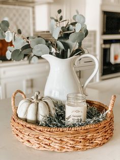 a wicker basket filled with white pumpkins and greenery on a kitchen counter