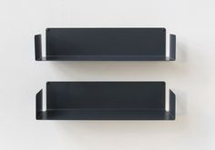 two black shelfs on the wall with one empty and one closed, both in different positions