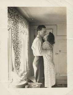 an old black and white photo of a man kissing a woman's forehead in front of a doorway