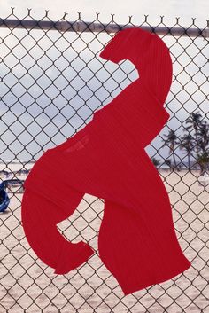 a red piece of art hanging on a chain link fence next to the ocean and beach