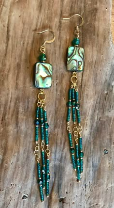 the earrings are made with green beads and gold chains on a piece of drift wood