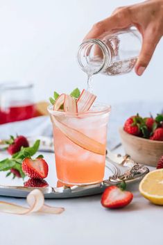 a person pouring a drink into a glass with strawberries and lemons around it