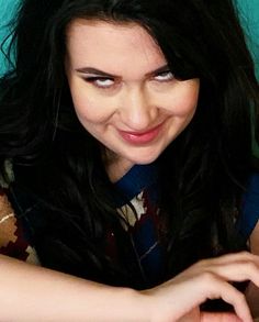 a woman is smiling while typing on her computer keyboard and holding a cell phone in her hand