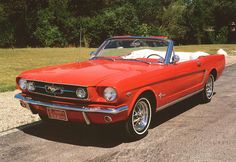 an old red mustang convertible parked on the side of the road