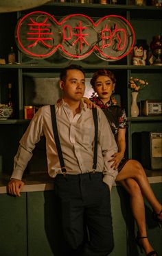 a man and woman standing next to each other in front of a bar with neon signs